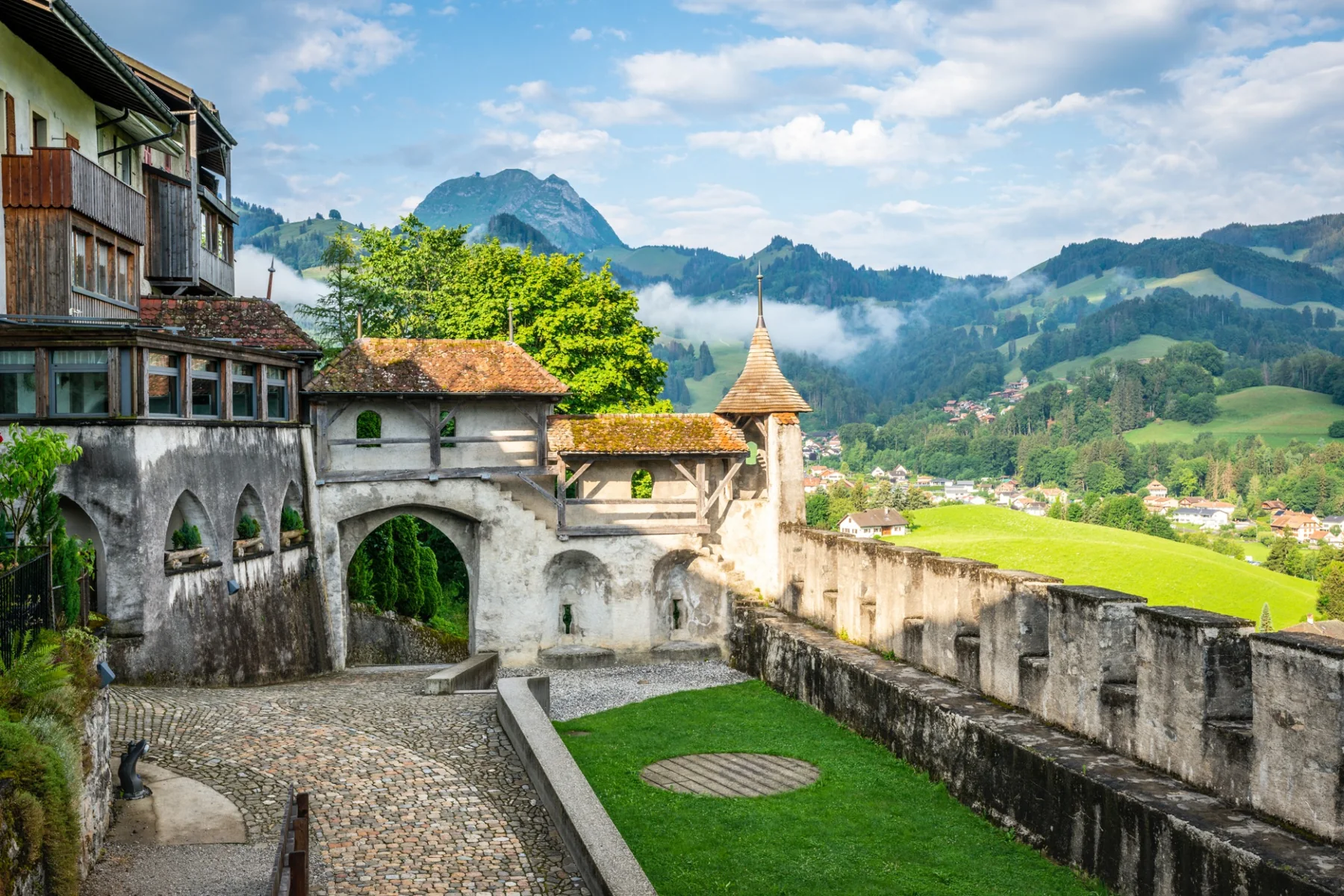 Patio empedrado del castillo de Gruyères con torre y montañas de los Prealpes al fondo